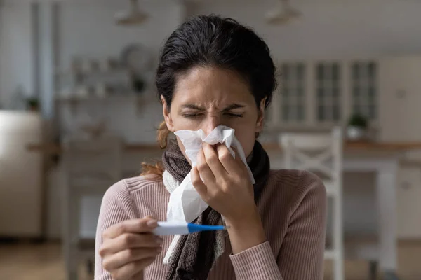 Закрыть больную женщину в шарфе, сморкающую нос, держащую термометр — стоковое фото