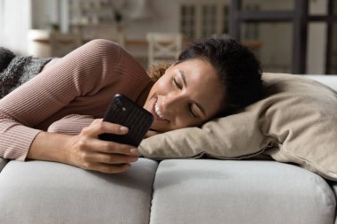 Akıllı telefon kullanan, kanepede dinlenen, gülümseyen kadını kapat.