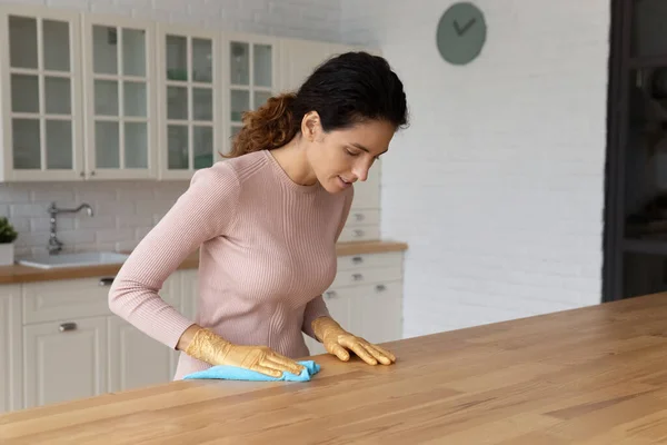 Молодая женщина в перчатках моет деревянный стол на современной кухне — стоковое фото