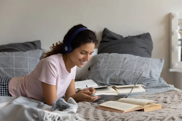 Donna sorridente in cuffia che studia online a casa, prendendo appunti — Foto Stock