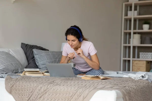 Mujer pensativa en auriculares inalámbricos que estudian en línea, sentado en la cama — Foto de Stock