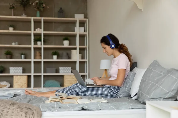 Mujer con auriculares usando laptop, estudiando en línea, sentada en la cama — Foto de Stock