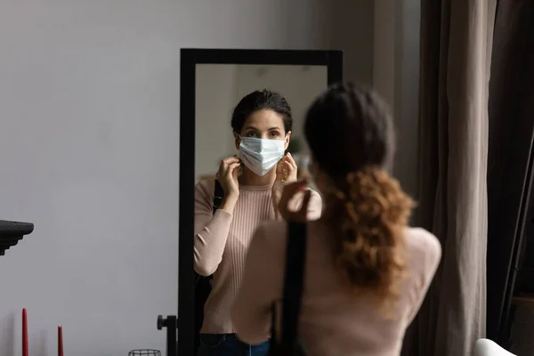 Mirror reflection of woman putting protective medical face mask — Stock Photo, Image