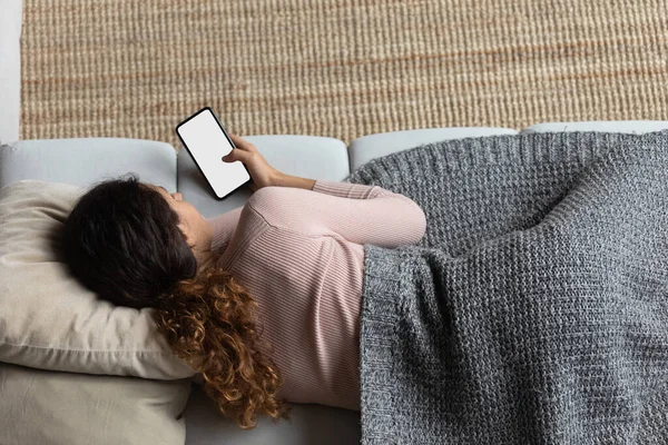 Vista superior de la mujer cubierta con manta relajante con teléfono inteligente — Foto de Stock