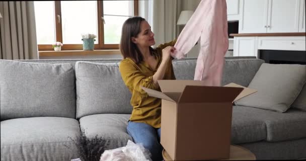 Счастливая молодая женщина распаковать посылку с блузкой удовлетворены качеством — стоковое видео