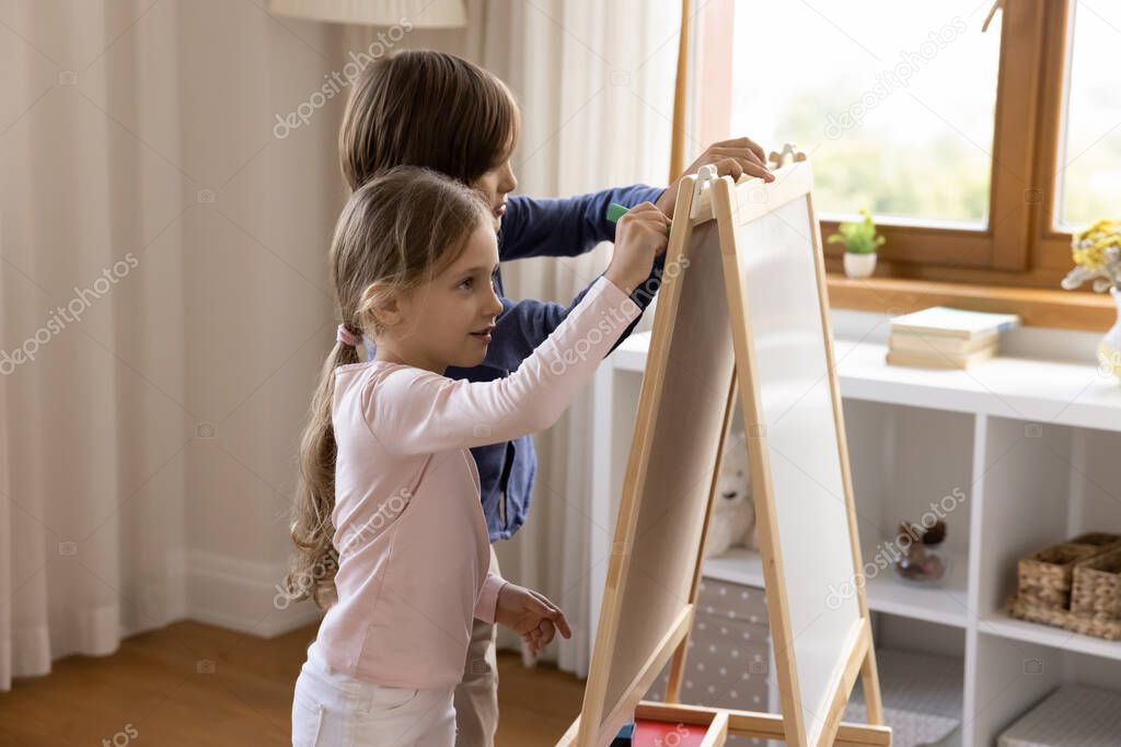 Two cute sibling kids drawing on toy small childish whiteboard