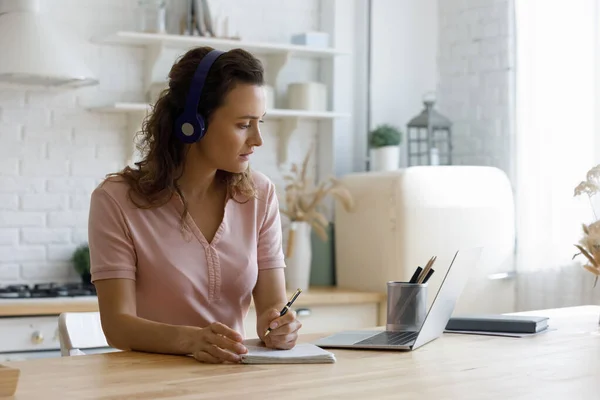 Focused student woman in wireless headphones writing notes at laptop — Stock Photo, Image