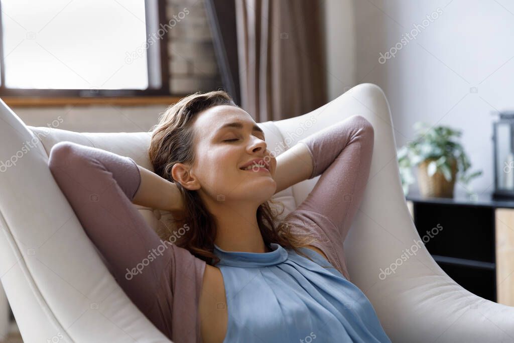 Happy peaceful homeowner girl resting in pale soft comfortable armchair