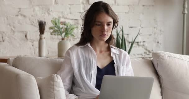 Mulher senta-se no sofá com laptop sente raiva devido mau funcionamento — Vídeo de Stock