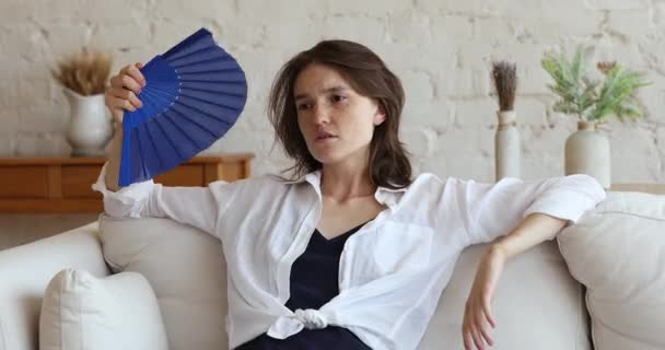 Вентилятор размахивания женщиной раздражен высокой температурой в гостиной — стоковое видео