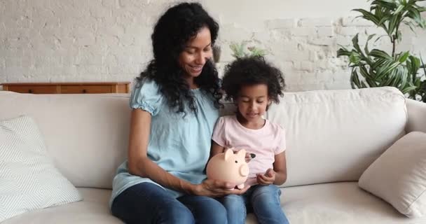 Menina africana e mãe conta cai moedas em mealheiro — Vídeo de Stock