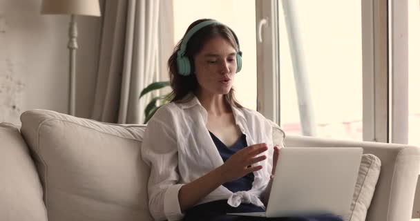 Жінка сидить на дивані з ноутбуком беруть участь у відеоконференції — стокове відео