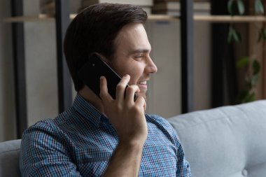 Oturma odasında koltukta oturan bir adam cep telefonuyla konuşuyor.