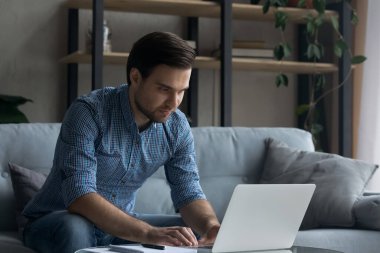 Evde dizüstü bilgisayarda çalışan yakışıklı bir genç.