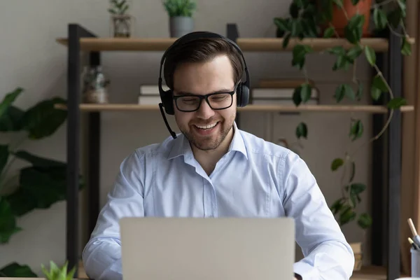 Hombre de negocios alegre en auriculares sentarse en el escritorio mira a la computadora portátil — Foto de Stock