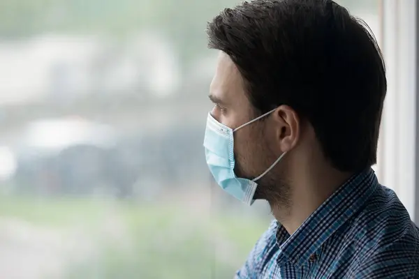 Man wear blue protective face mask looks out window — Stock Photo, Image