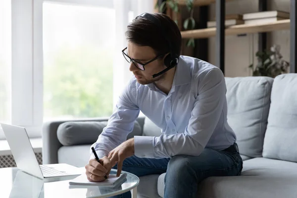 Mladý podnikatel nosit sluchátka poslouchat audio kurz píše v copybooku — Stock fotografie