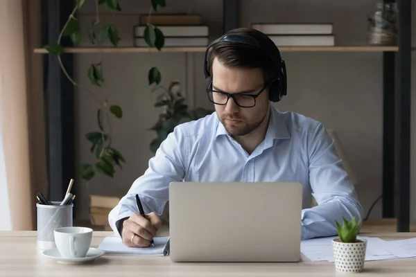 Man in headphones sit at desk holds pen noting information — Stock Photo, Image