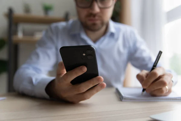 Homme assis au bureau tient stylo, smartphone écrit dans le bloc-notes — Photo