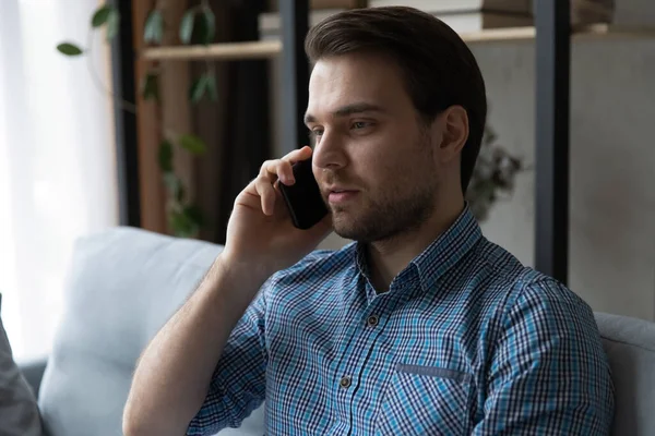 Mladý muž sedí na pohovce a mluví na mobilu — Stock fotografie