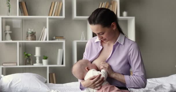 Junge Mutter sitzt auf Bett und füttert Säugling mit Brust — Stockvideo