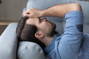 Kanepede yatan genç adam baş ağrısından muzdarip.