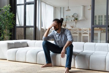 Afrikalı adam kanepede oturuyor. Dokunaklı kafa umutsuz görünüyor.