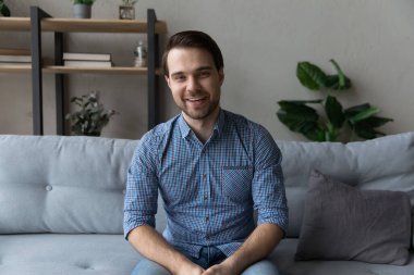 Gülümseyen genç adam kanepeye oturur ve kameraya bakar.