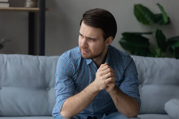 Man having mental pain, sit on sofa looks into distance