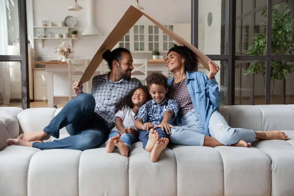 African family sit on couch under cardboard roof — Stock Photo, Image