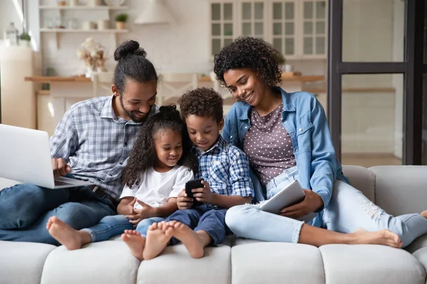 Afrikaanse familie met kinderen zitten op de bank met diverse apparaten — Stockfoto