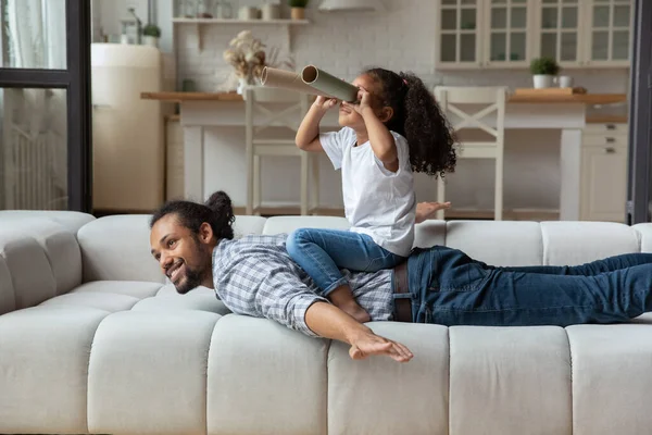 Afrikansk flicka sitter på pappa tillbaka tittar in i pappersrör — Stockfoto