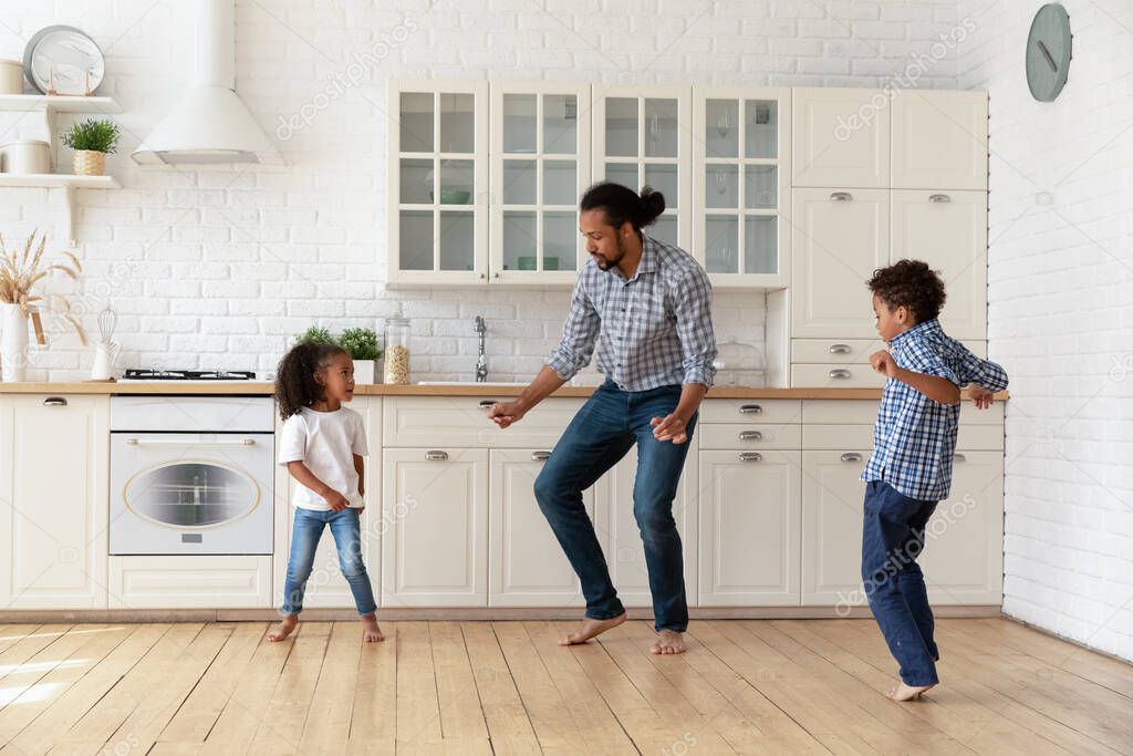 Active African father and cute children dancing in the kitchen