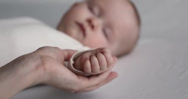 Huzurlu bebek kestirirken şefkatli anne avucunu okşuyor.