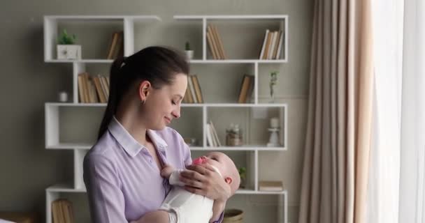 Giovane madre che cammina per il soggiorno dondolando bambino in braccio — Video Stock