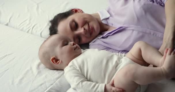 Mami acostada en la cama viendo al bebé pateando piernas en el aire — Vídeo de stock