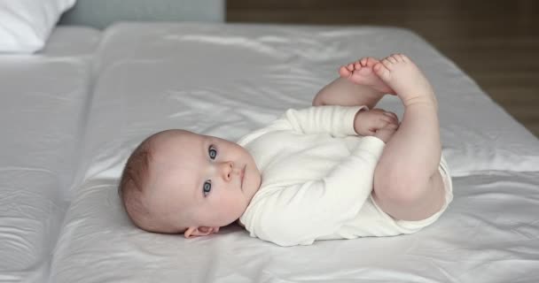 Baby klädd i singel liggande på sängen rörliga ben leende — Stockvideo