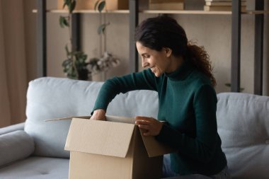 Heyecanlı genç bir kadın online alışveriş kutusunu açıyor.