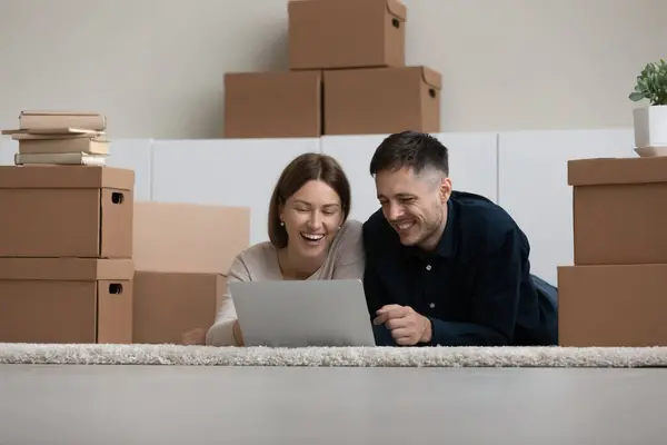 Feliz riéndose joven familia pareja utilizando la computadora, la planificación de decoraciones. — Foto de Stock
