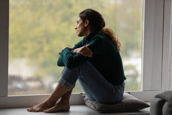 Pensive Latino woman relax at home looking in window