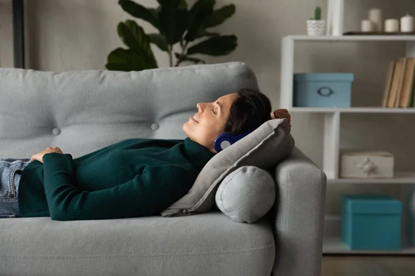 Glückliche Frau entspannt sich auf Sofa und hört Musik über Kopfhörer — Stockfoto