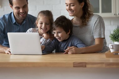 Evde dizüstü bilgisayar kullanan iki çocuklu mutlu ebeveynler.