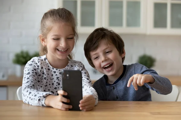 Alegre hermana pequeña y hermano usando el teléfono inteligente, divertirse —  Fotos de Stock