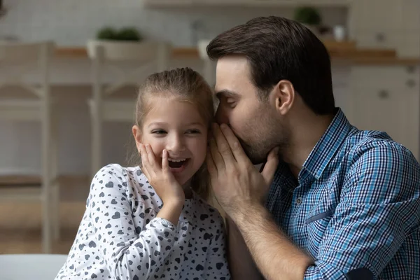 Захоплена маленька дівчинка і батько діляться секретами, шепочучи в вухо — стокове фото