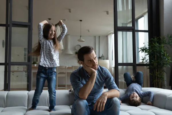 Cansado padre sentado en el sofá con ruidosa hija e hijo — Foto de Stock