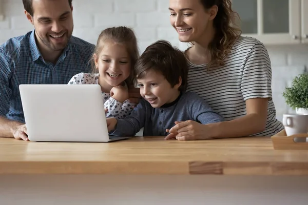 Evde dizüstü bilgisayar kullanan iki çocuklu mutlu ebeveynler.