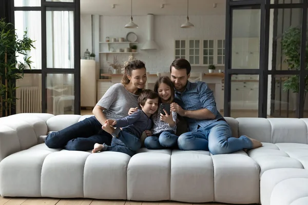 Çocuklu mutlu bir aile akıllı telefon kullanıyor, birlikte kanepede oturuyorlar.