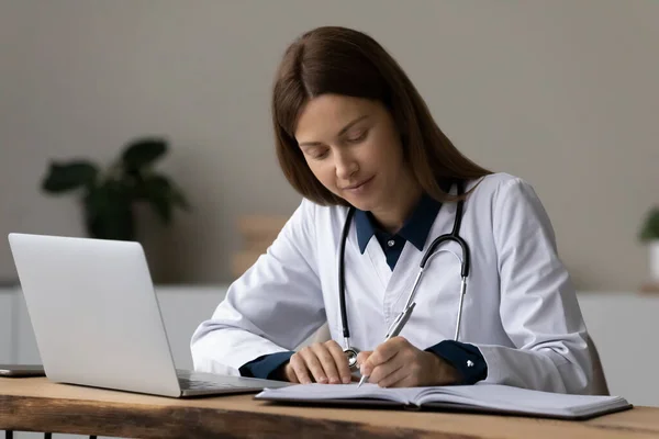 Koncentrerad ung kvinnlig läkare antecknar på arbetsplatsen — Stockfoto