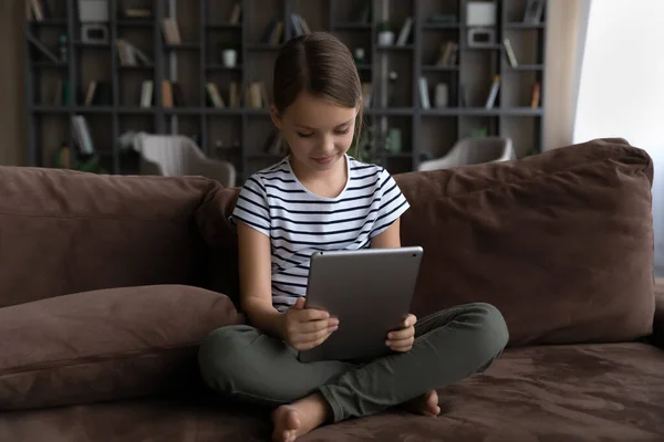 Curious preteen girl sit on sofa alone hold digital pad — Stock Photo, Image