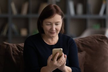 Odaklanmış olgun bir kadın koltuğa oturur akıllı telefondan mesaj yazar.